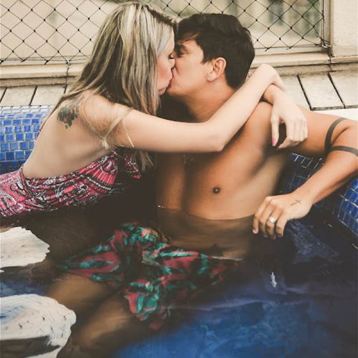 Photo of a couple kissing in a swimming pool, the man's shirtless, wearing floral swim shorts, the woman's wearing a floral swimsuit.